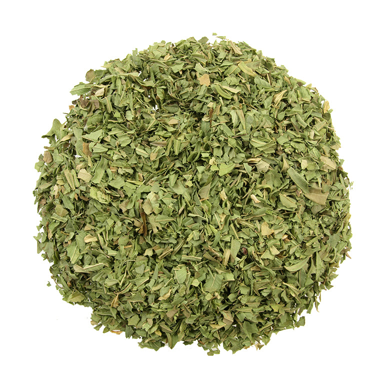 A heap of dried, chopped green herbs from Bondi Beach Tea Cos Organic Lemon Verbena Tea is set against a white backdrop, showcasing its leafy texture and green shades that offer a soothing, caffeine-free experience known for aiding digestion gently.