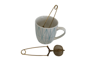A white mug with a blue geometric pattern holds a Clamp Style Tea Infuser, and an extra strainer sits beside it—ideal for savoring your favorite Bondi Beach Tea Co blend.