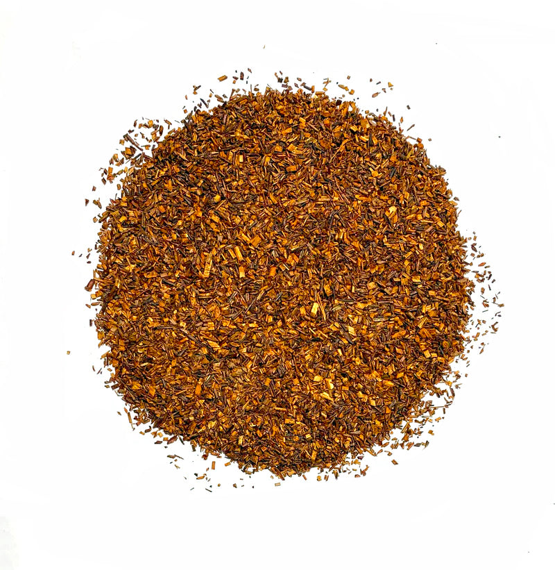 A circular pile of Bondi Beach Tea Cos Pure Organic Rooibos Tea rests on a white background, showcasing small, flat, reddish-brown leaves that create a textured look, representing the antioxidant-rich and caffeine-free qualities of the brew.