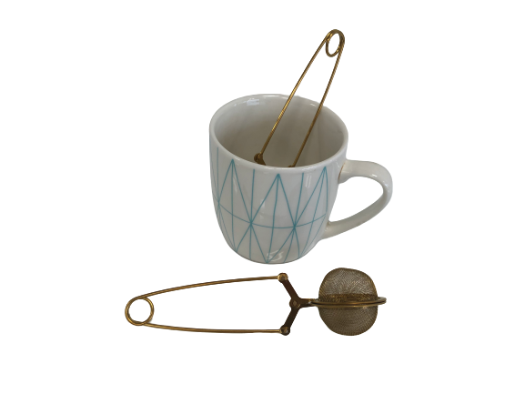 A white mug with a blue geometric pattern holds a Clamp Style Tea Infuser, and an extra strainer sits beside it—ideal for savoring your favorite Bondi Beach Tea Co blend.